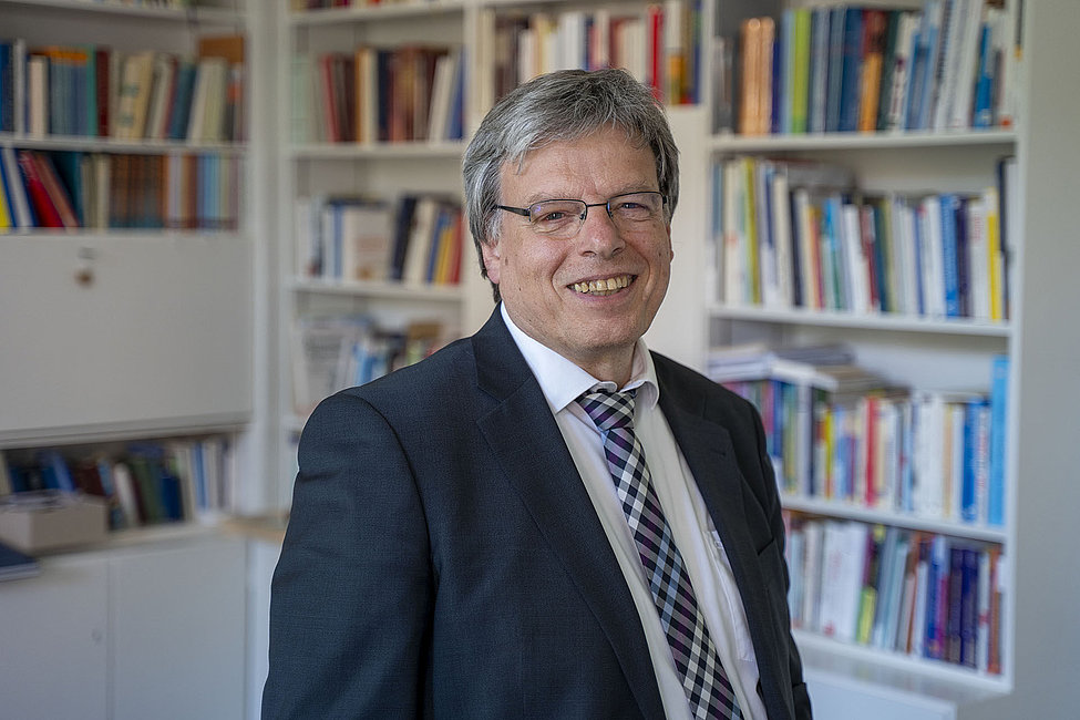Lächelnder Mann im Anzug und Krawatte vor Bücherregal